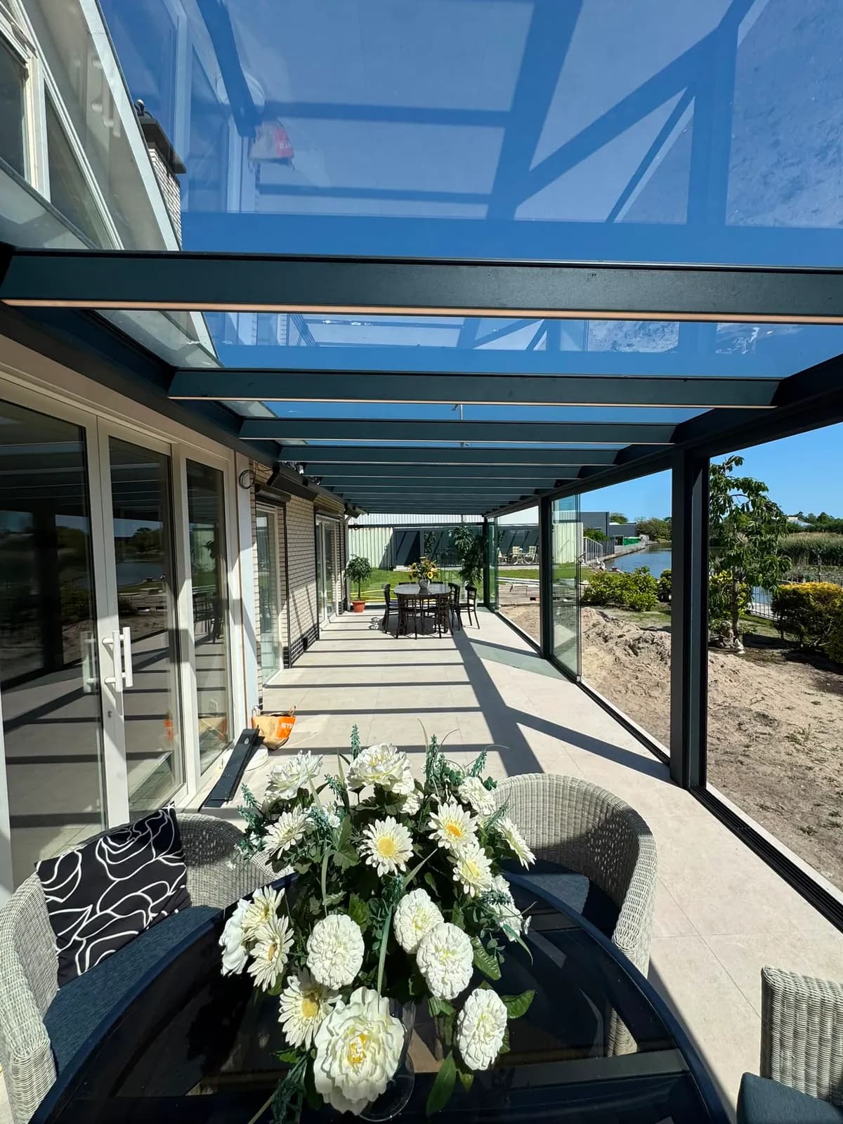 Lange veranda met glazen dak langs een woning aan het water