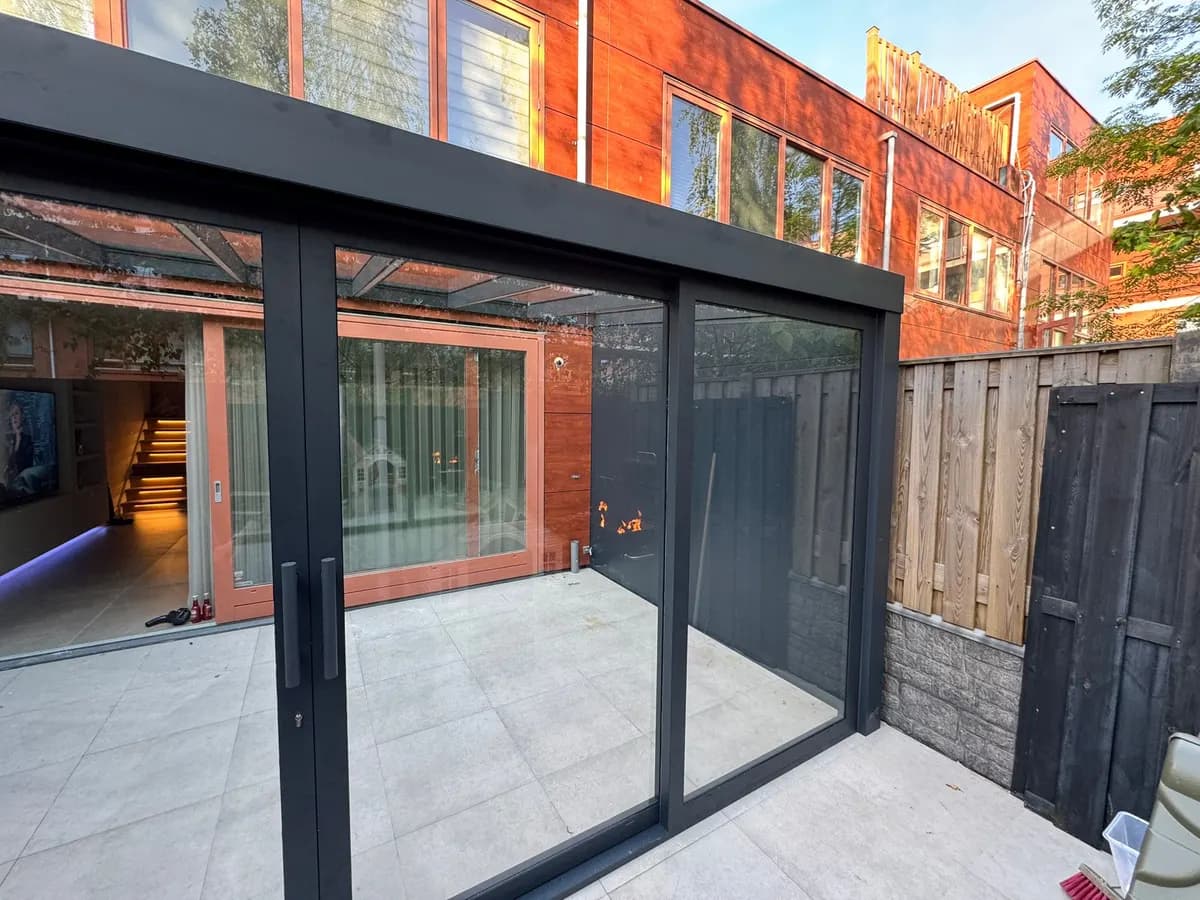 Glazen schuifwand met glasdak tegen een moderne gevel